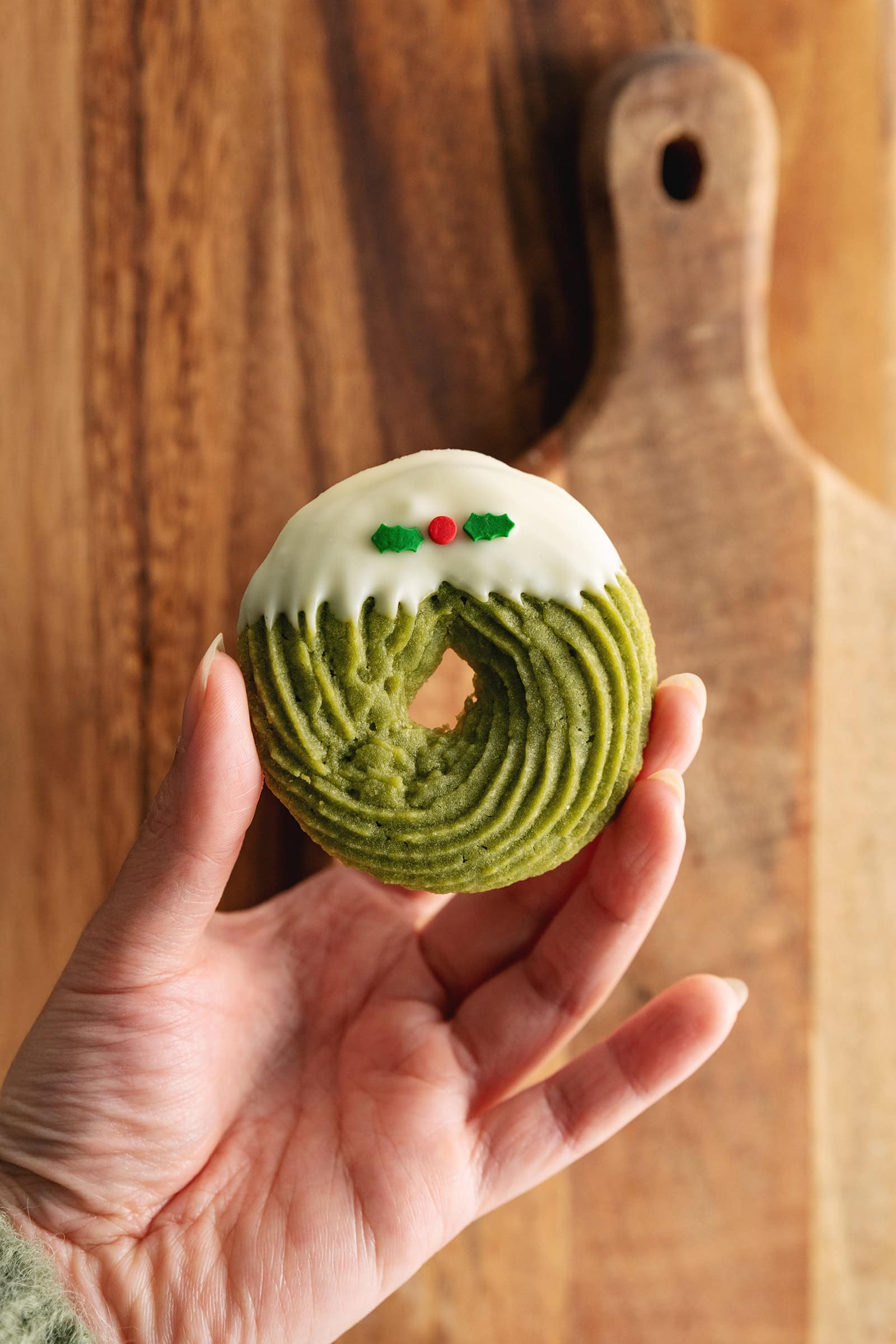 A hand holding a matcha butter cookie dipped in white chocolate in front of wooden boards.