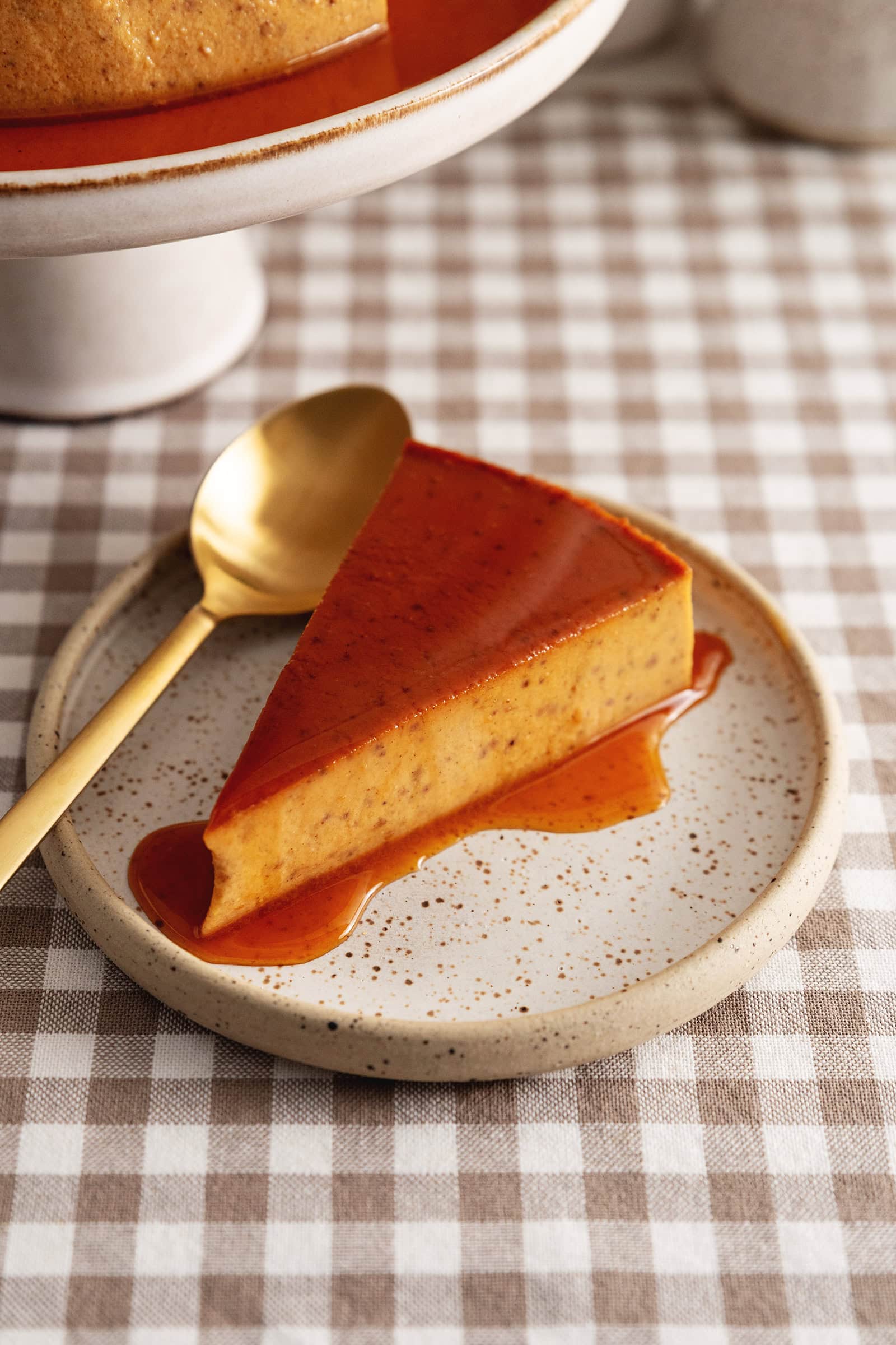 A slice of pumpkin flan on a plate topped with caramel sauce.