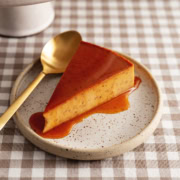 A slice of pumpkin flan on a plate topped with caramel sauce.