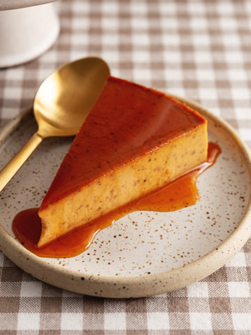A slice of pumpkin flan on a plate topped with caramel sauce.