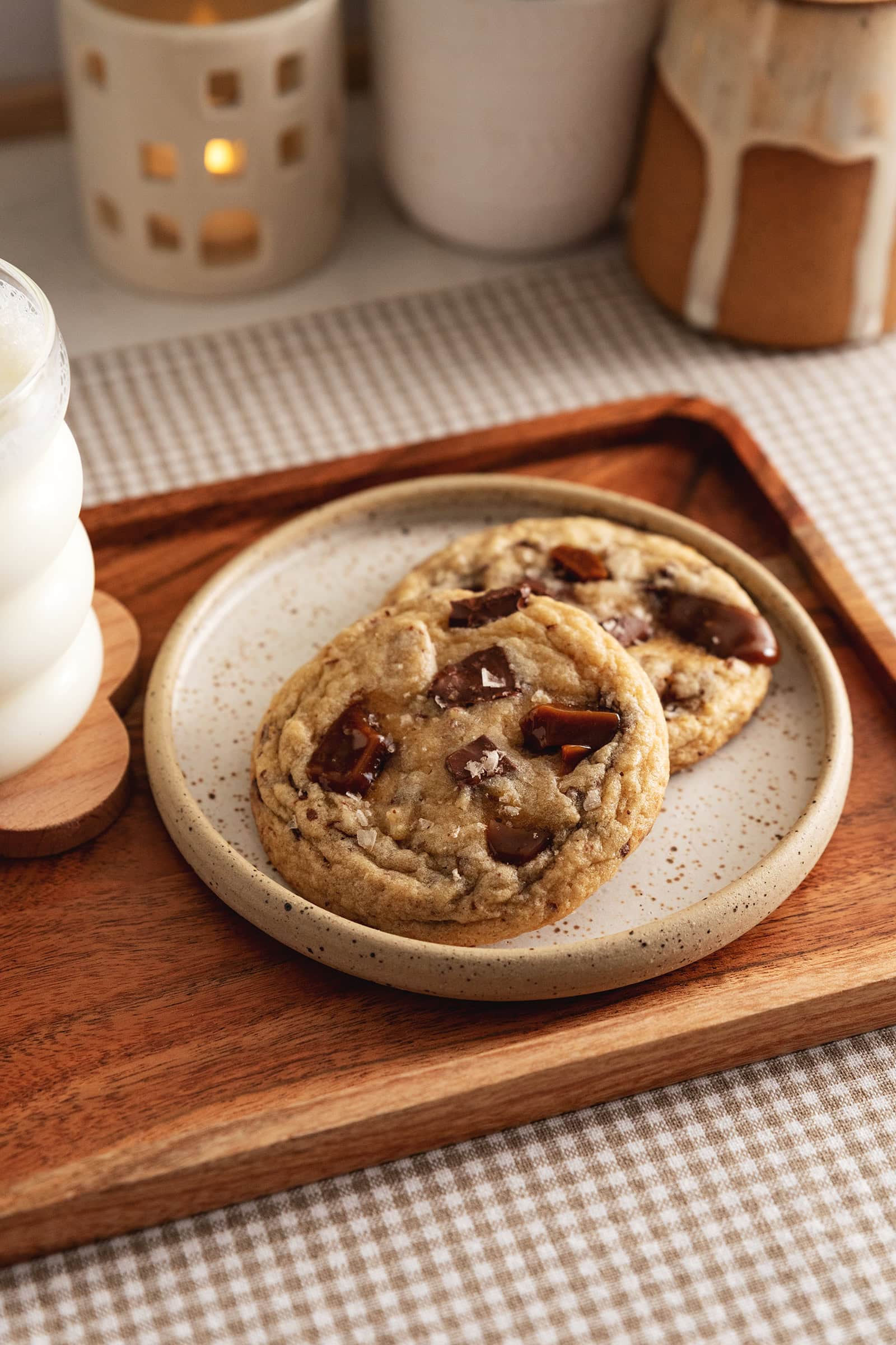Two toffee cookies on a plate with a glass of milk beside them.