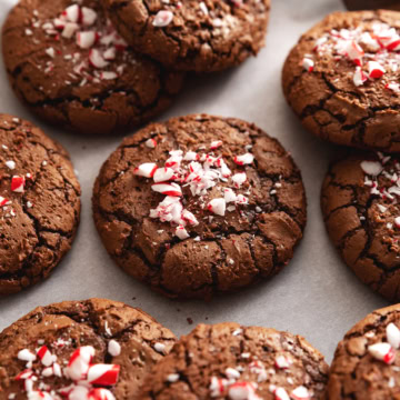 Several chocolate peppermint cookies with crushed candy canes on top scattered on parchment paper.