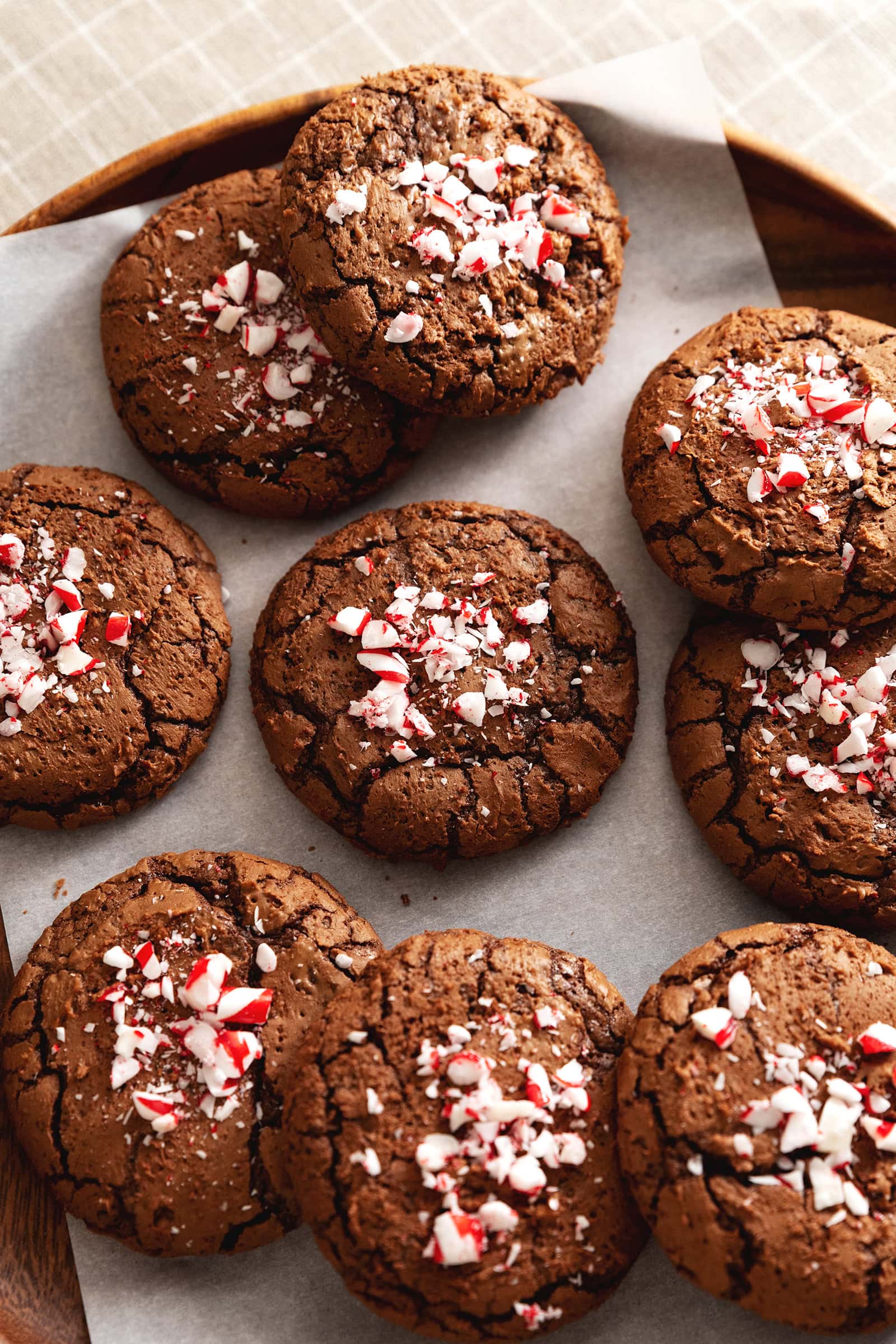 Several chocolate peppermint cookies with crushed candy canes on top scattered on parchment paper.