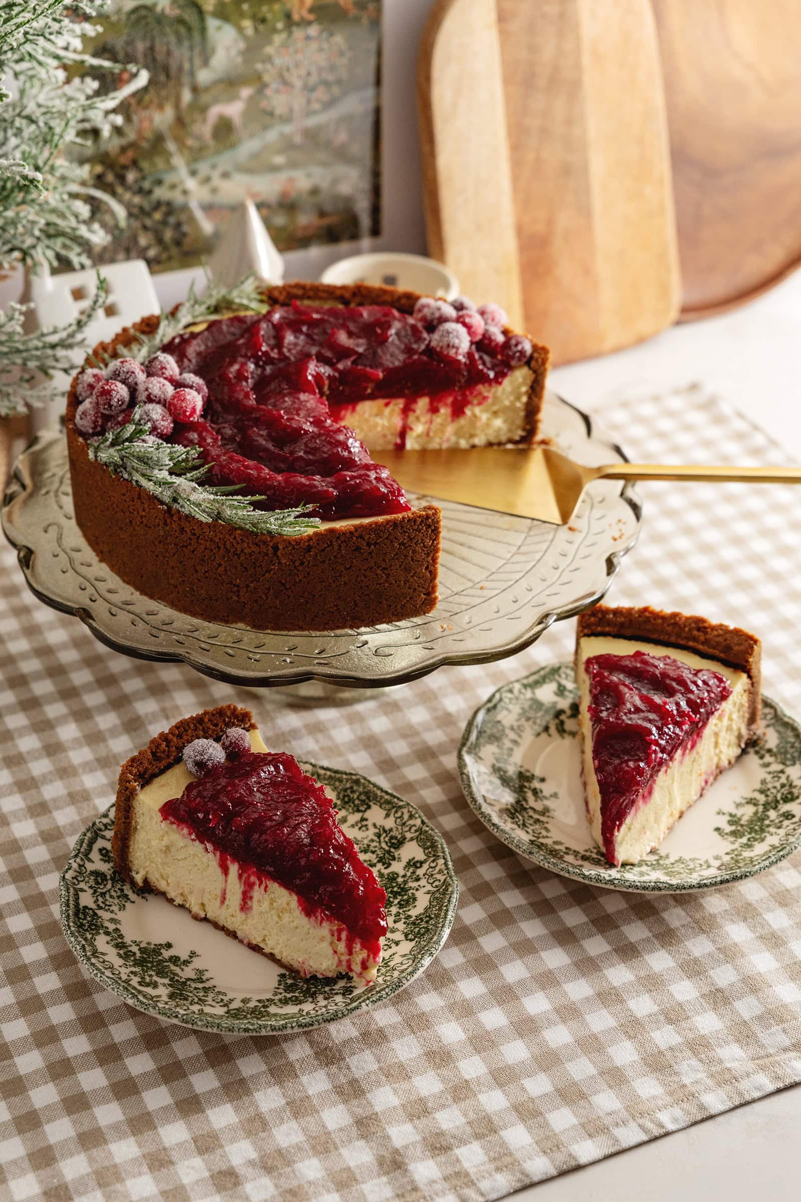 Two slices of cranberry orange cheesecake on plates in front of the rest of the cake on a cake stand.