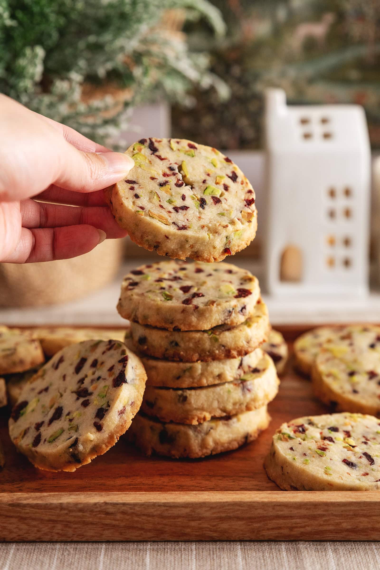 A hand holding a cranberry pistachio shortbread cookies on top of a stack of cookies.