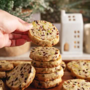 A hand holding a cranberry pistachio shortbread cookies on top of a stack of cookies.