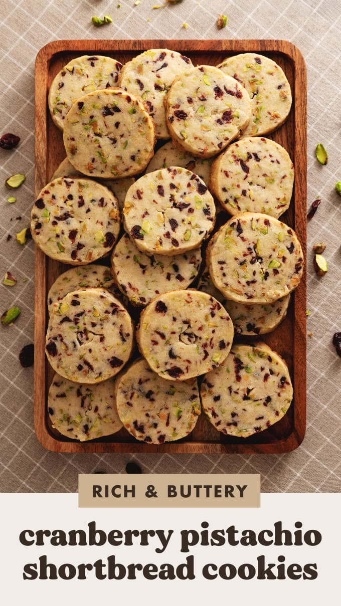 A wooden platter full of cranberry pistachio shortbread cookies stacked on top of each other.
