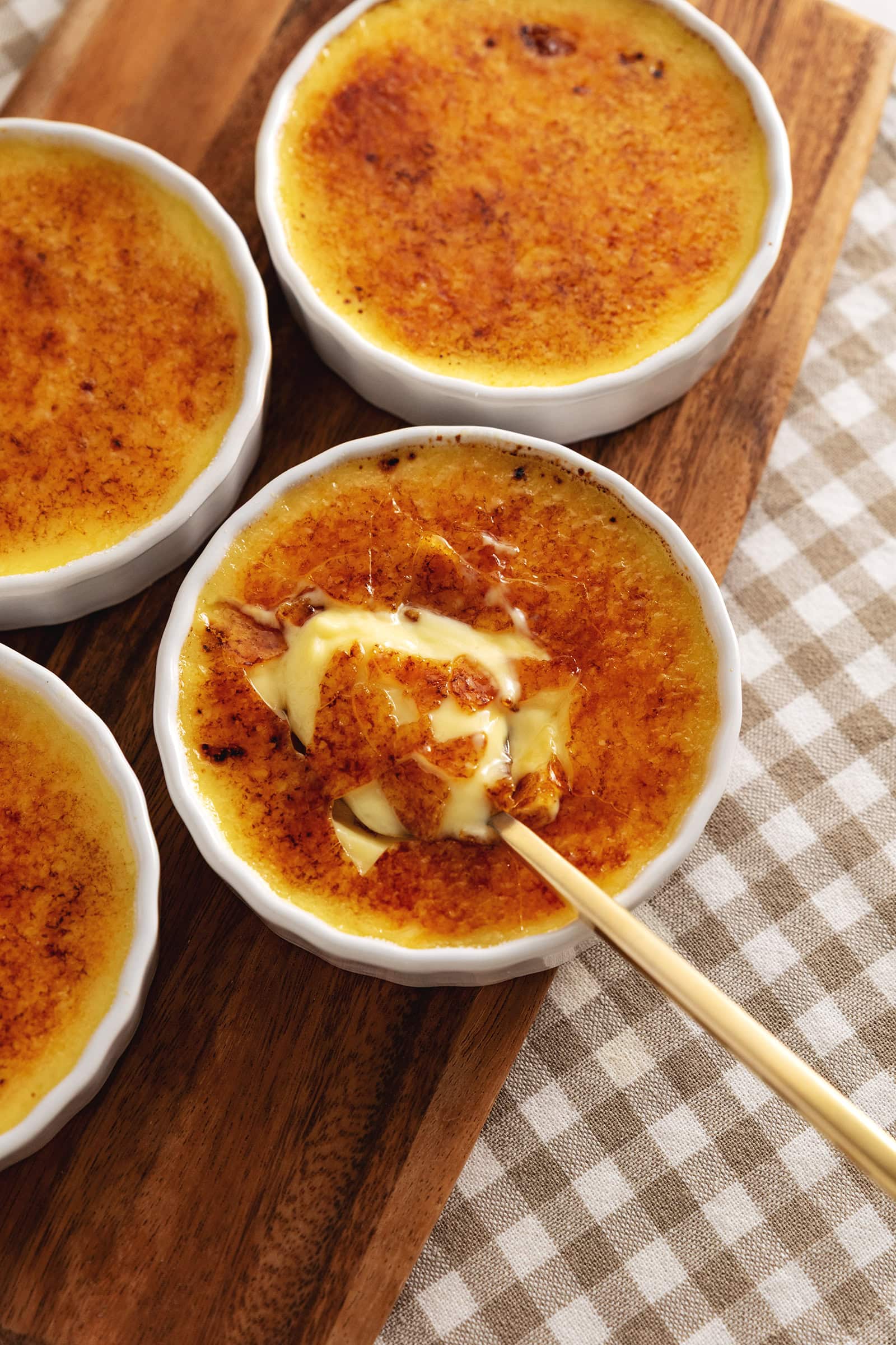 Four ramekins of eggnog crème brûlée with a spoon resting in the custard of one ramekin.
