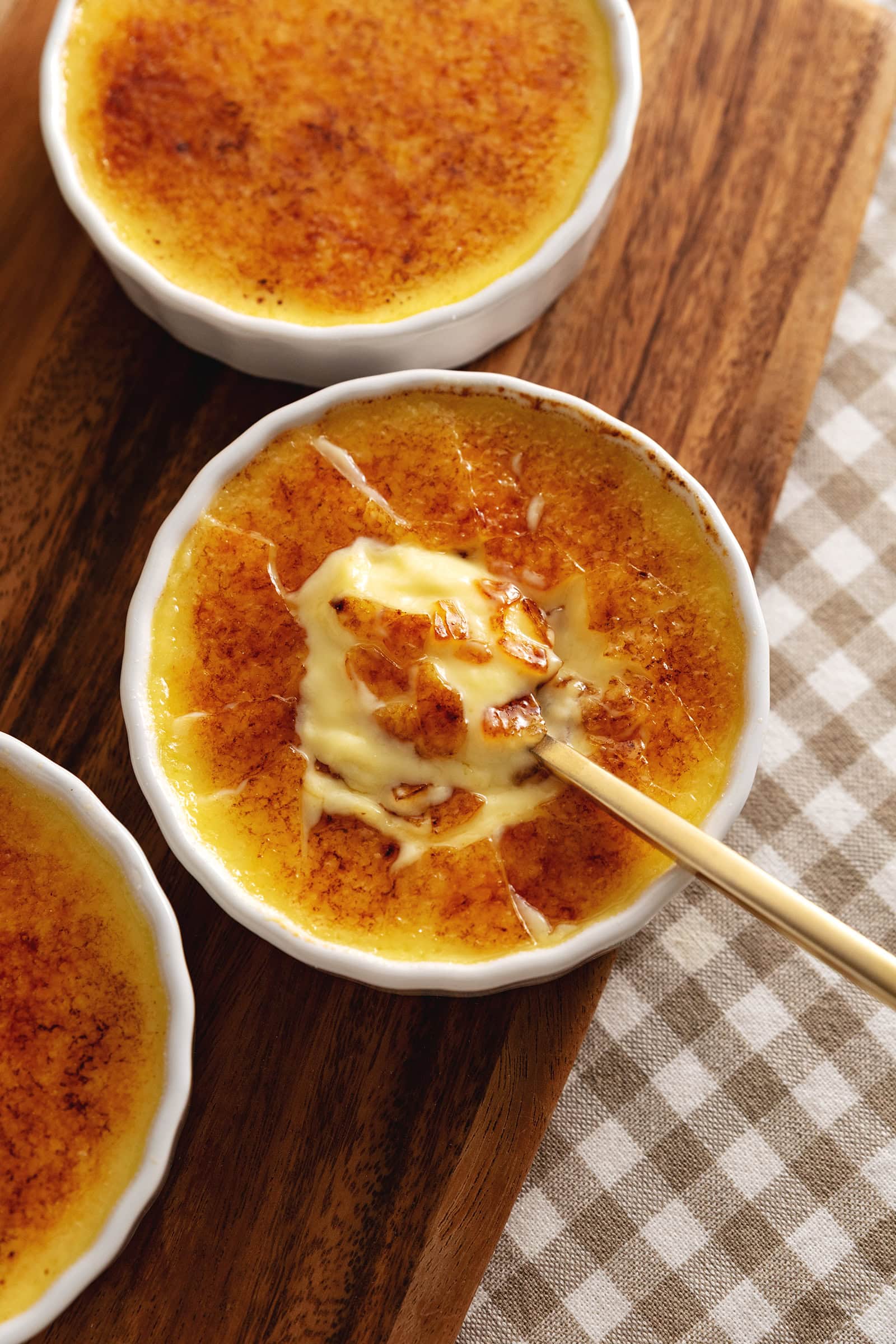 A ramekin of eggnog crème brûlée with a spoon resting in the custard under the crunchy sugar shards.