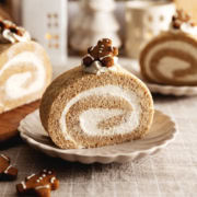 A slice of gingerbread roll cake on a plate with a gingerbread man cookie on top.