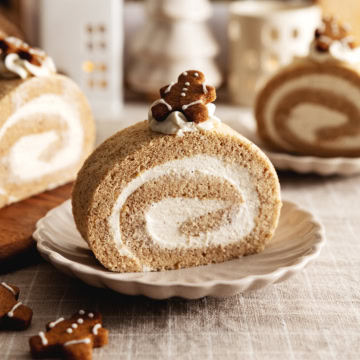 A slice of gingerbread roll cake on a plate with a gingerbread man cookie on top.