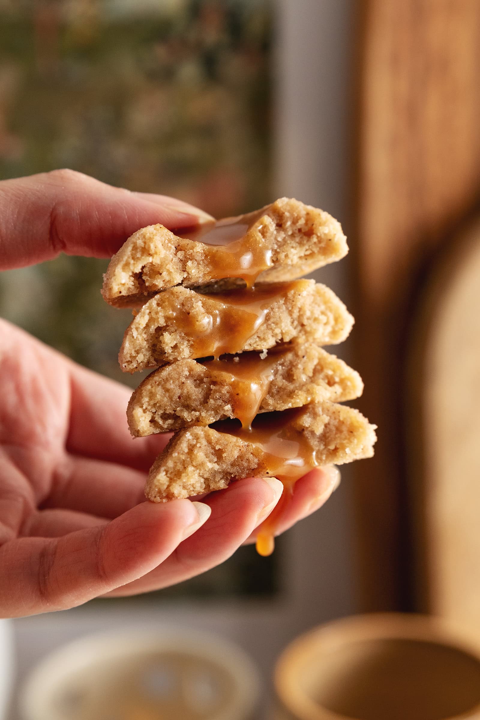 Hand holding a stack of gingerbread thumbprint cookies cut in half with caramel running down the middle.