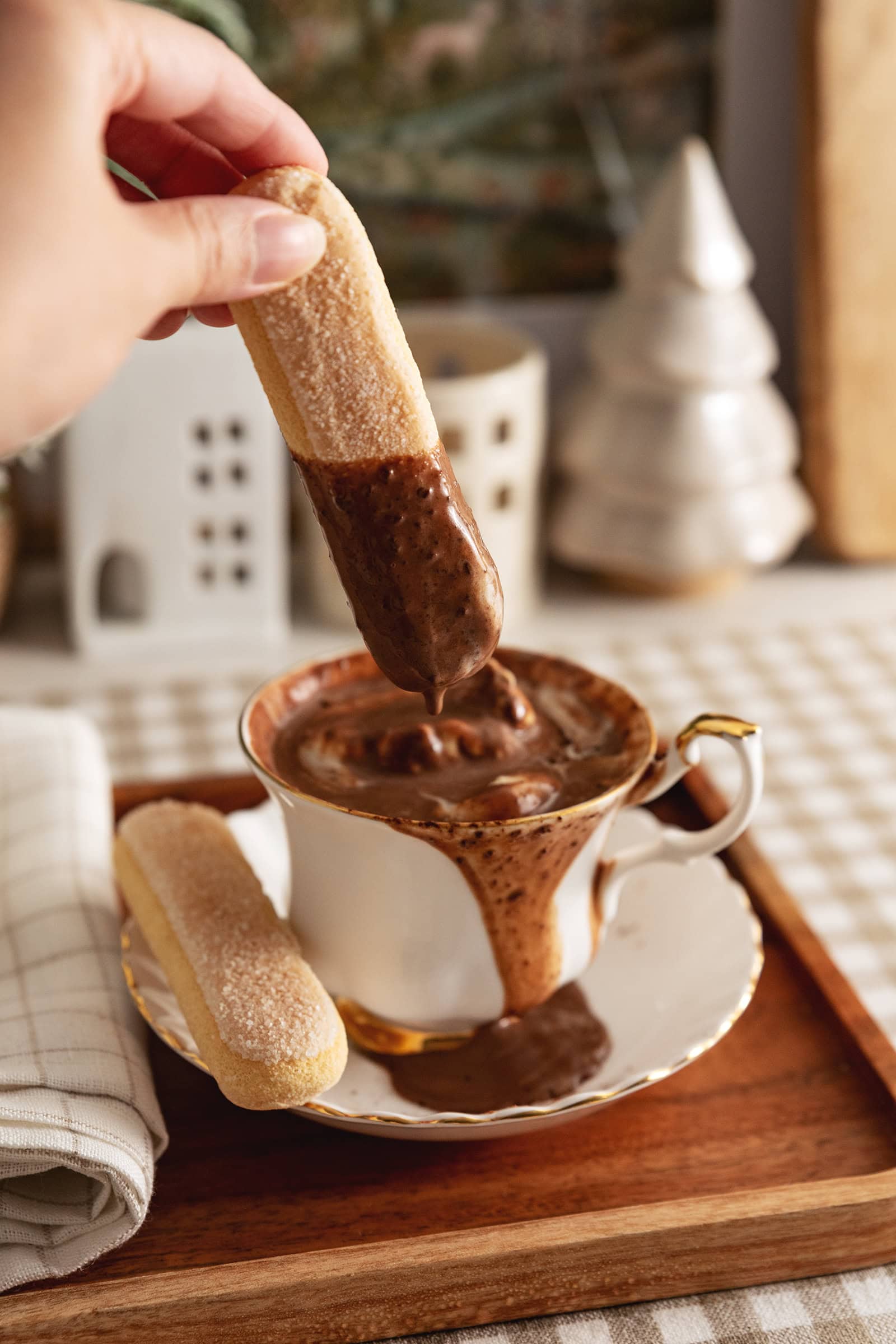 Hand dipping a ladyfinger into a teacup of tiramisu hot chocolate.