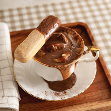 A ladyfinger dipped in tiramisu hot chocolate resting on the edge of the teacup.