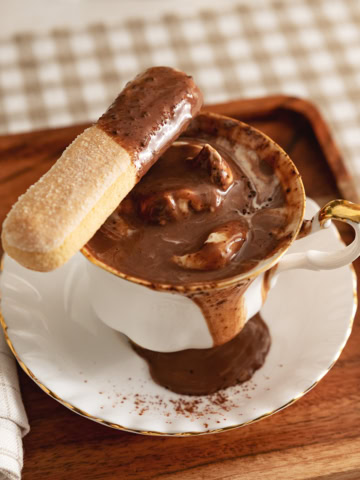 A ladyfinger dipped in tiramisu hot chocolate resting on the edge of the teacup.